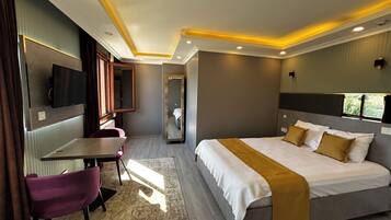 Quarto de hotel moderno com uma cama grande, uma escrivaninha, uma cadeira, uma TV fixada na parede e um espelho.