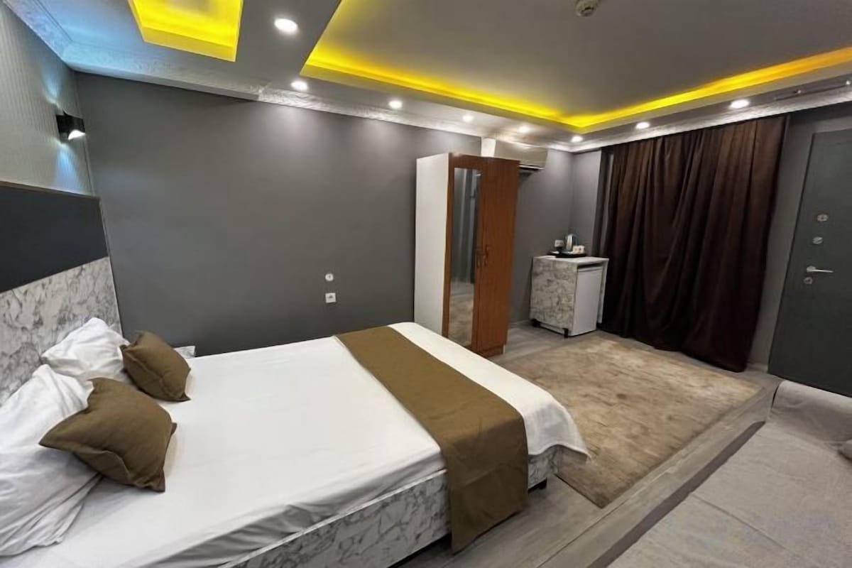 A modern hotel room with a large bed, a desk, and a wardrobe.