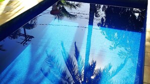 A swimming pool with a tiled edge and a clear blue water surface reflecting palm tree silhouettes. - Residence Solemare Buzios (Búzios)