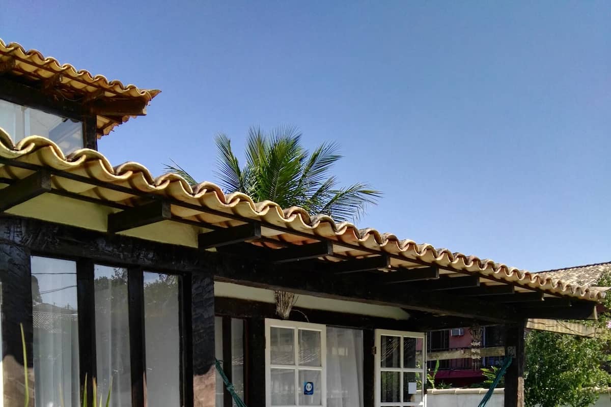 Une maison avec un toit en tuiles, un hamac et un jardin rempli de fleurs et de plantes.