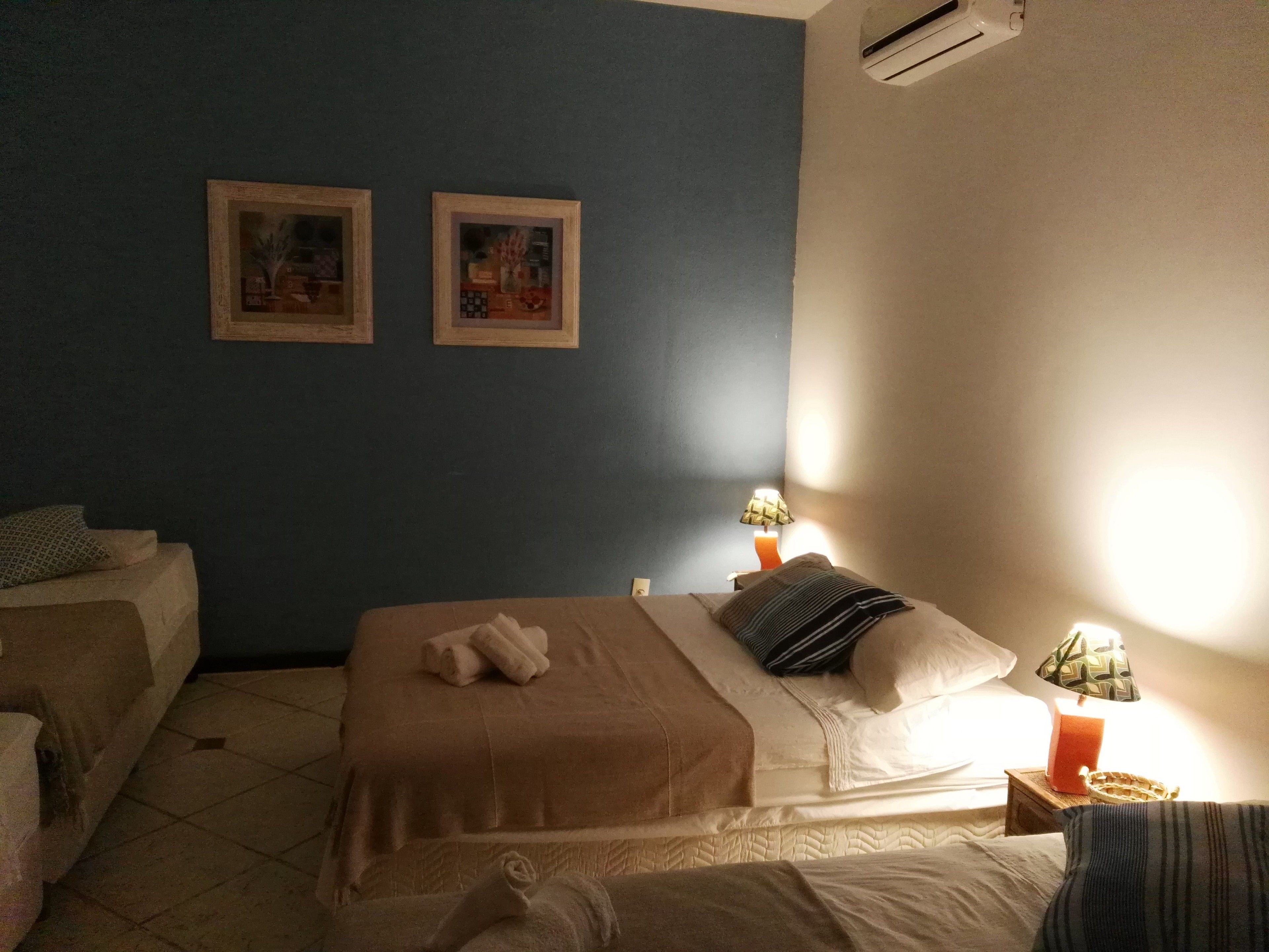 A hotel room with a bed, two wall-mounted pictures, a nightstand with a lamp, and a tiled floor.