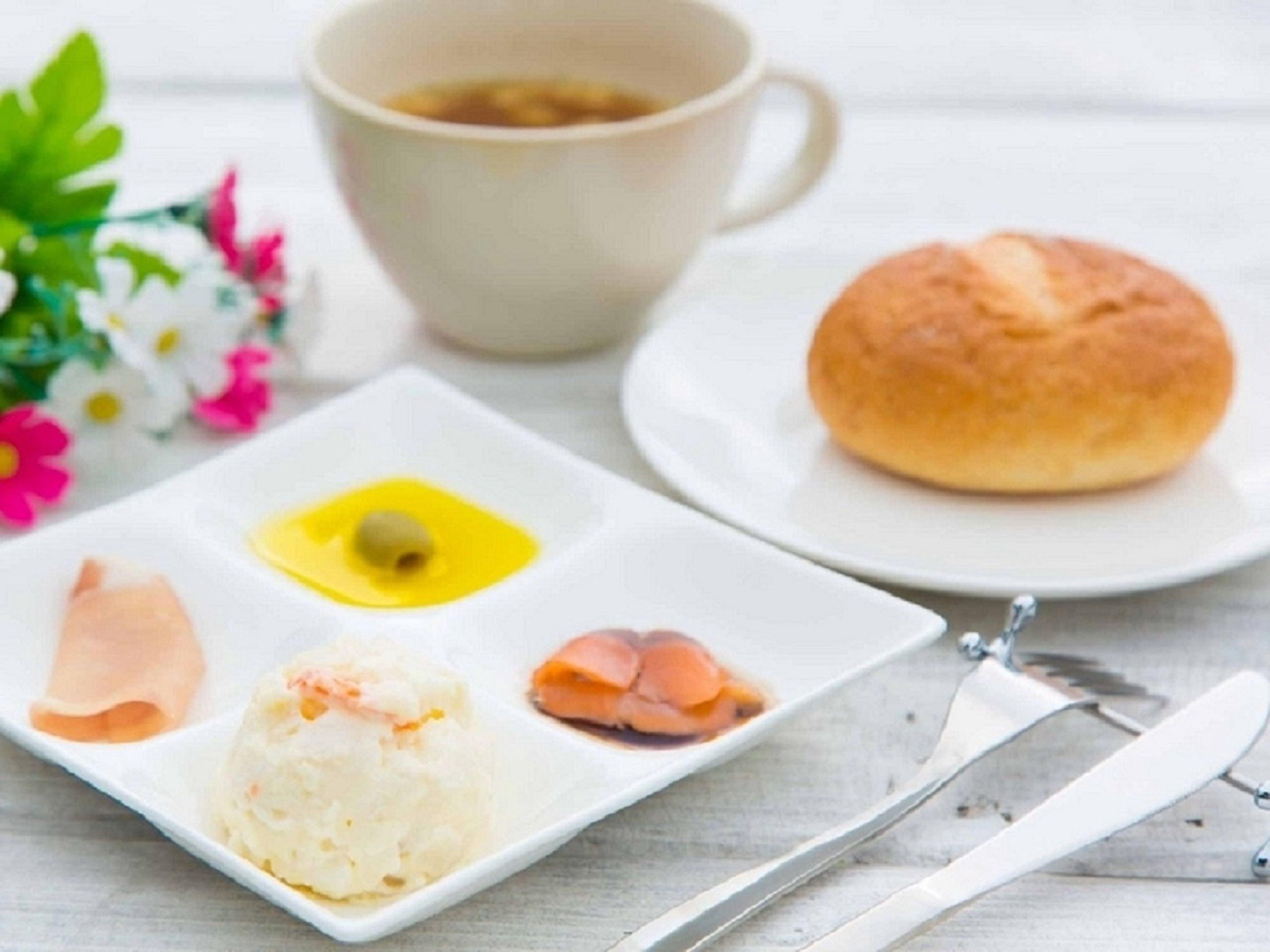 A plate with food items, a cup of tea, and a bun on a table.