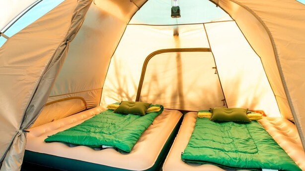 Een tent met twee bedden, elk met een groene deken en kussen.