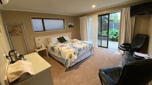 A hotel room with a bed, a desk, a chair, a TV, and a sliding glass door to the outside. - BigSky Bed and Breakfast (Omarama)