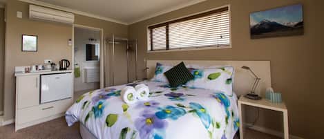 A bedroom with a bed, a nightstand, a desk, and a bathroom.