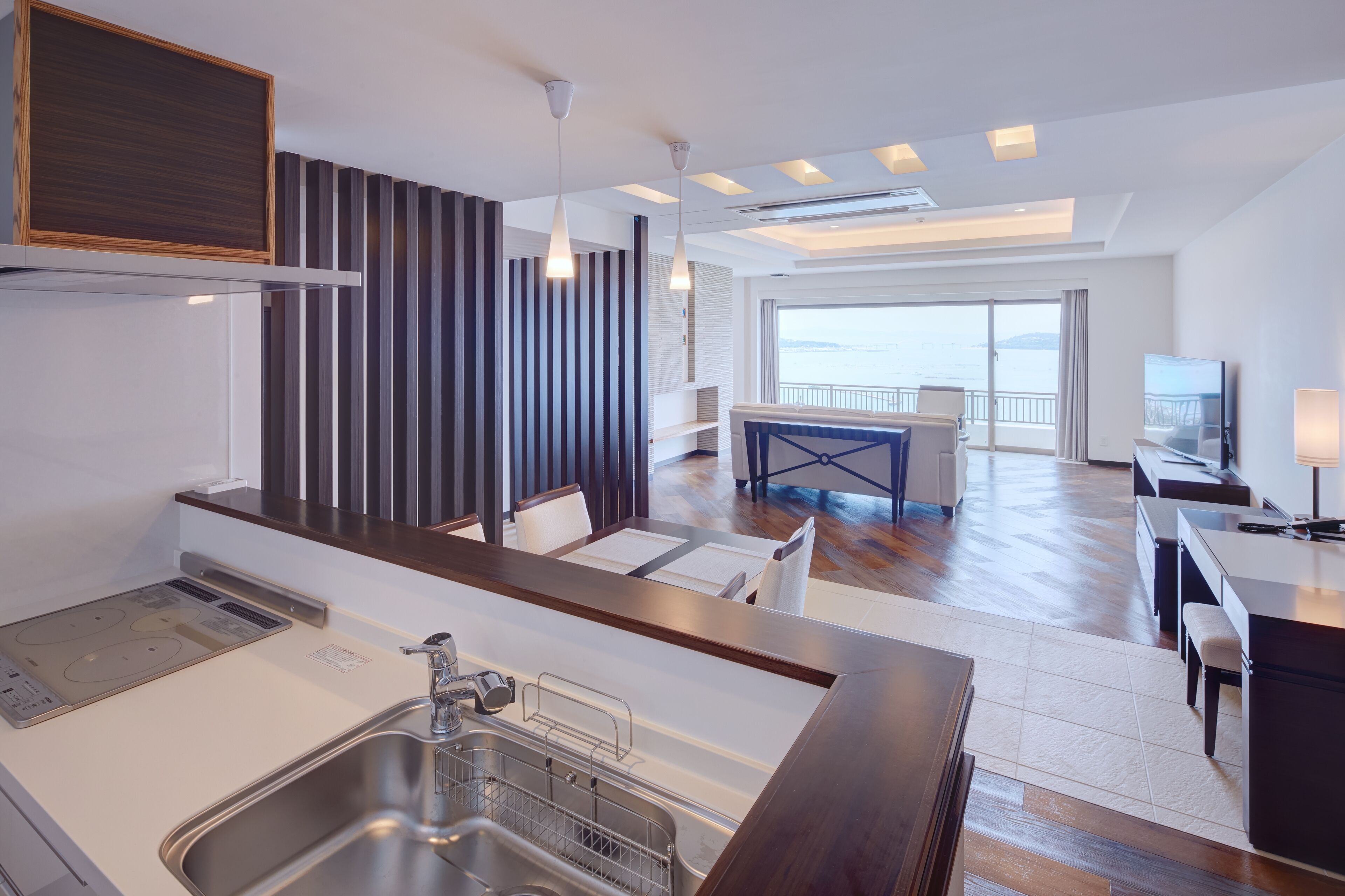 Een moderne keuken met een inbouwspoelbak, een zithoek met tafel en stoelen, en uitzicht op zee door grote ramen.
