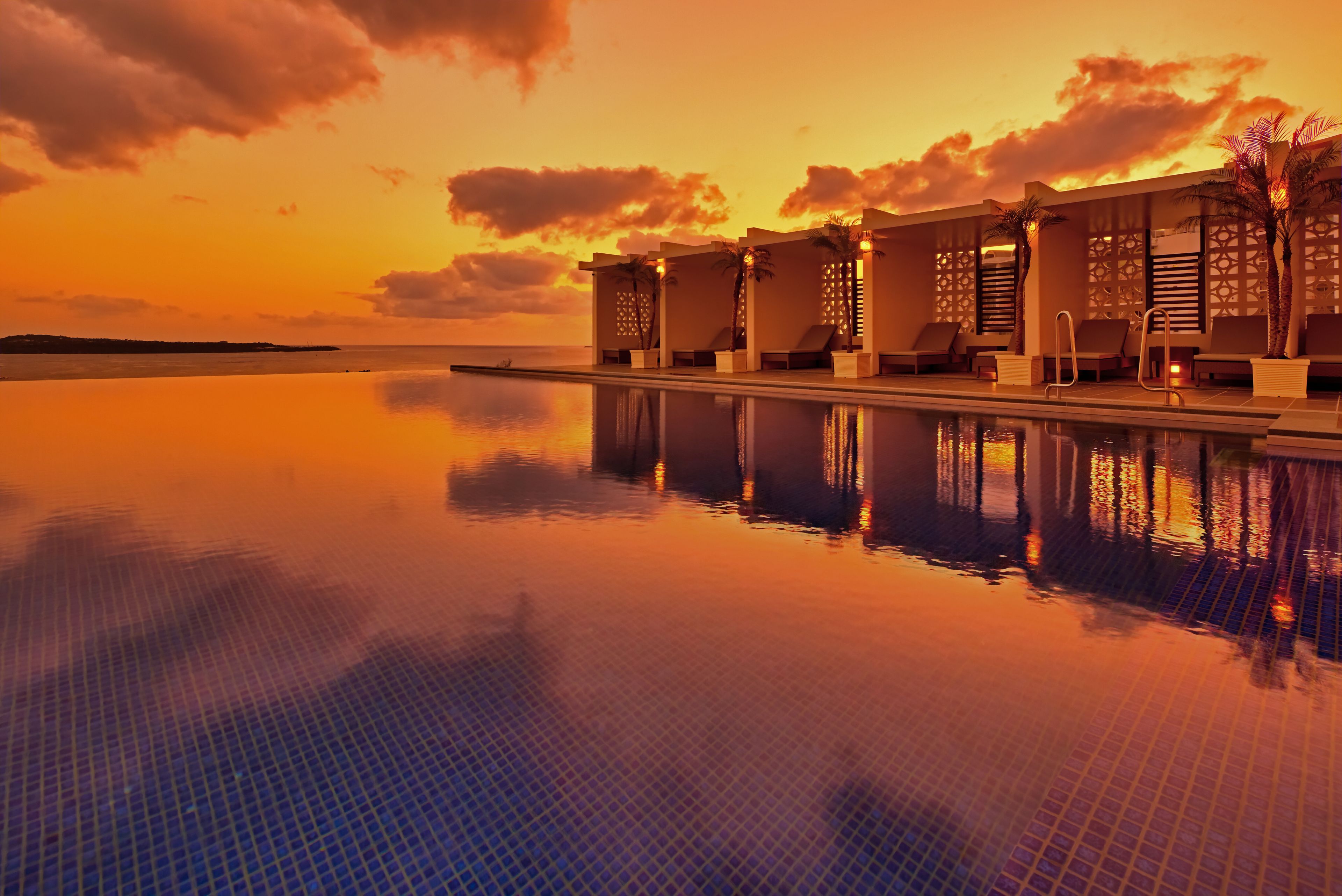 A poolside area with lounge chairs and a view of the ocean at sunset.