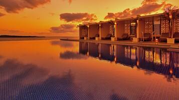 A poolside area with lounge chairs and a view of the ocean at sunset.
