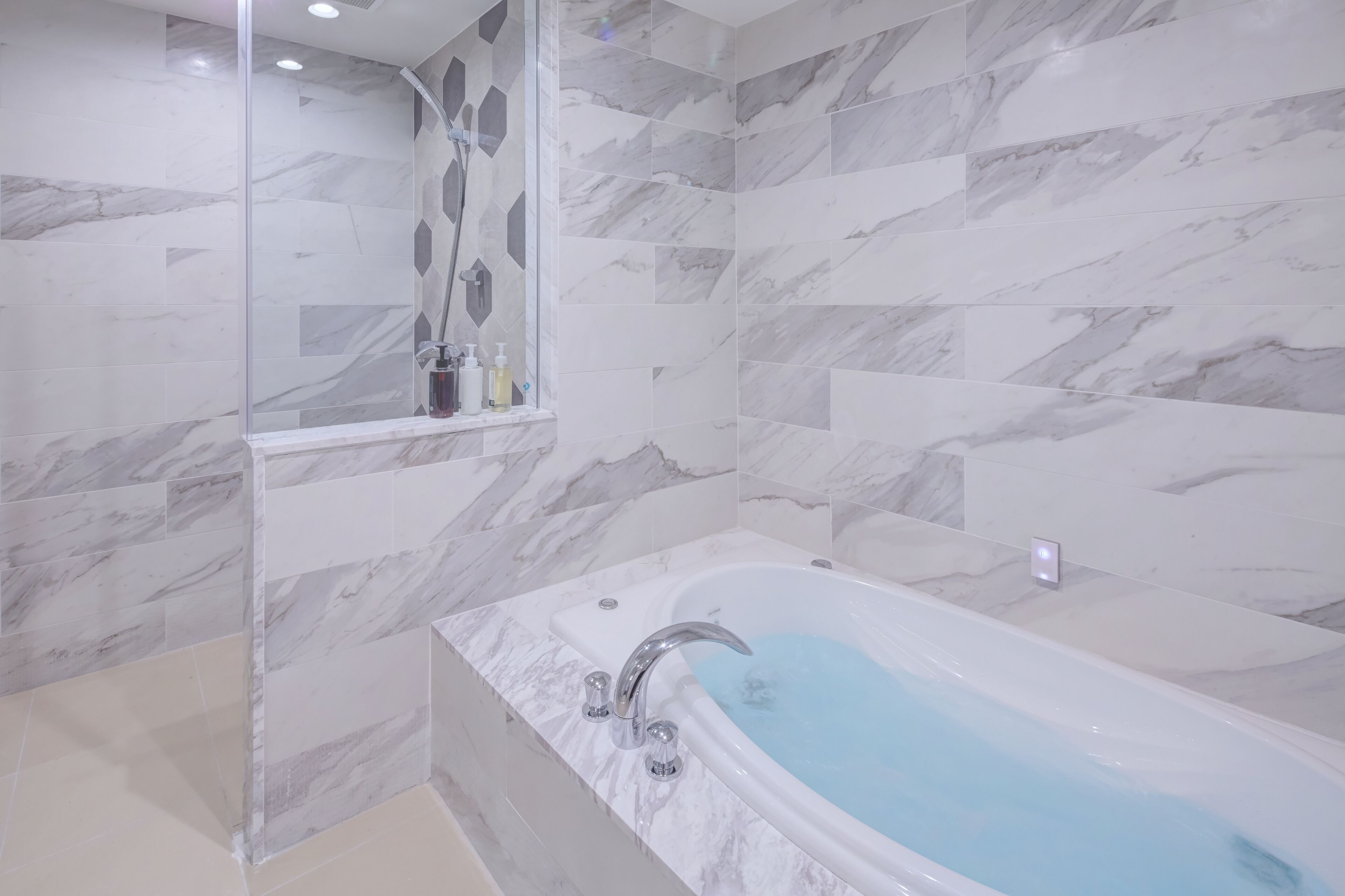 A modern bathroom with a marble-tiled shower and a bathtub with a built-in seat.