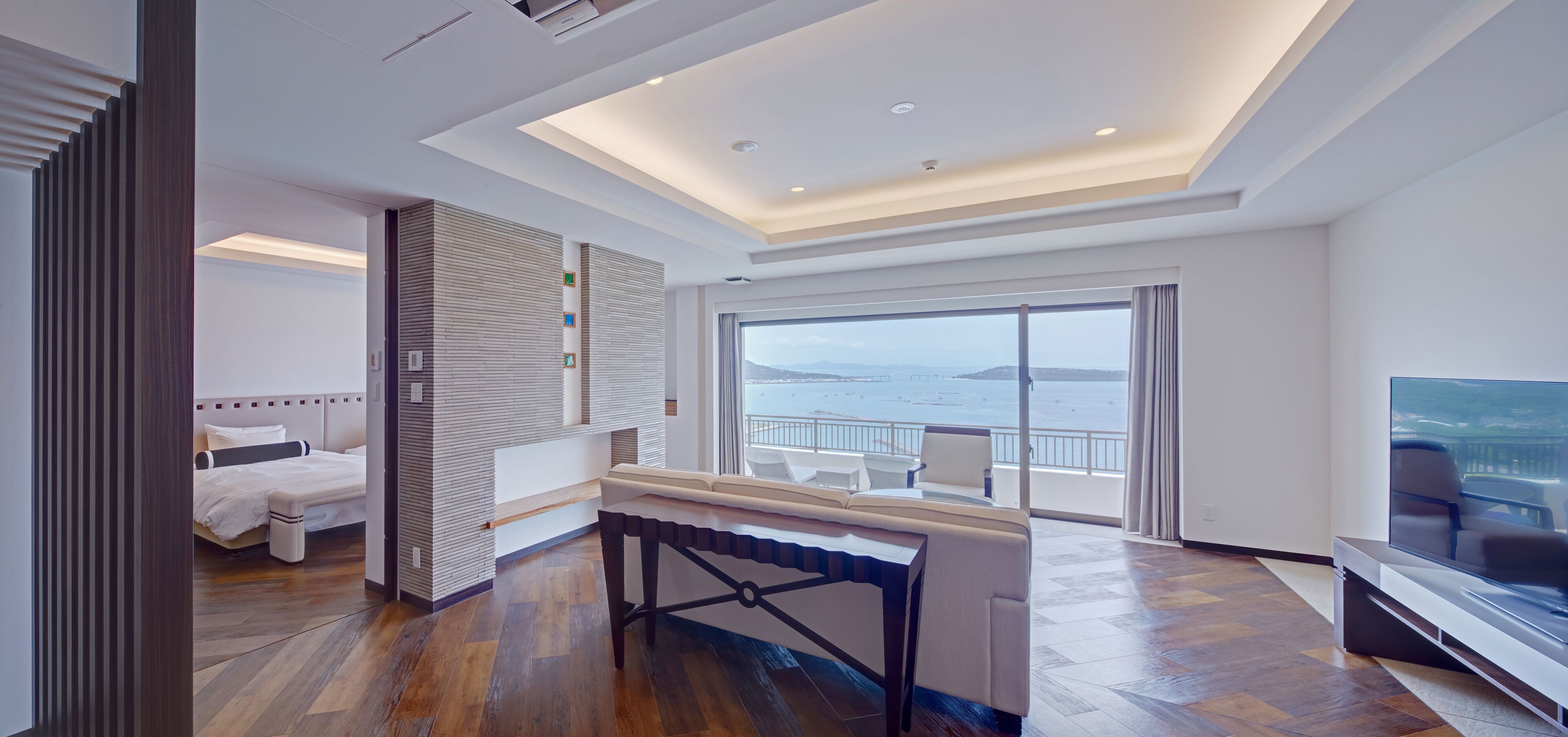 A modern hotel room with a large balcony, a bed, a desk, and a TV.