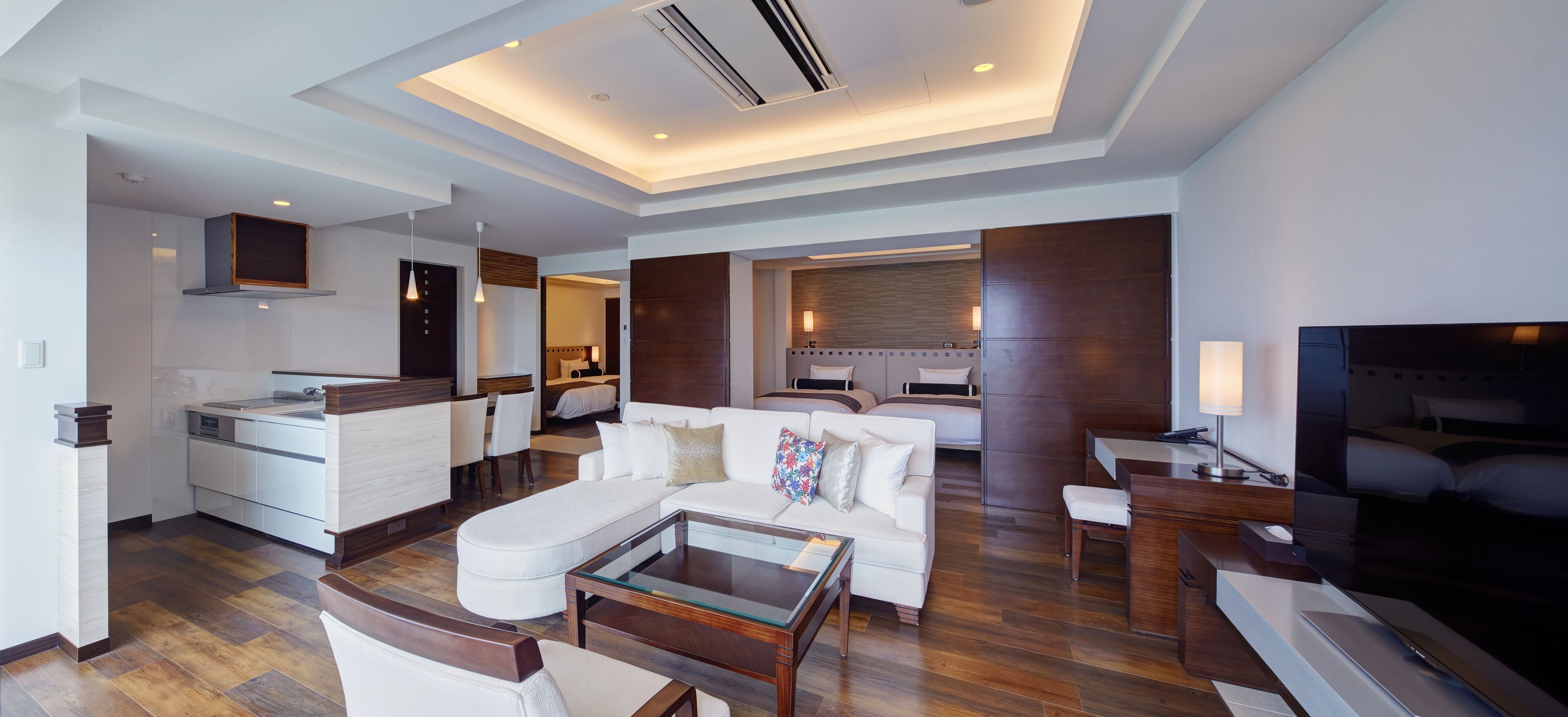 A modern hotel room with a living area, kitchenette, and a separate bedroom.