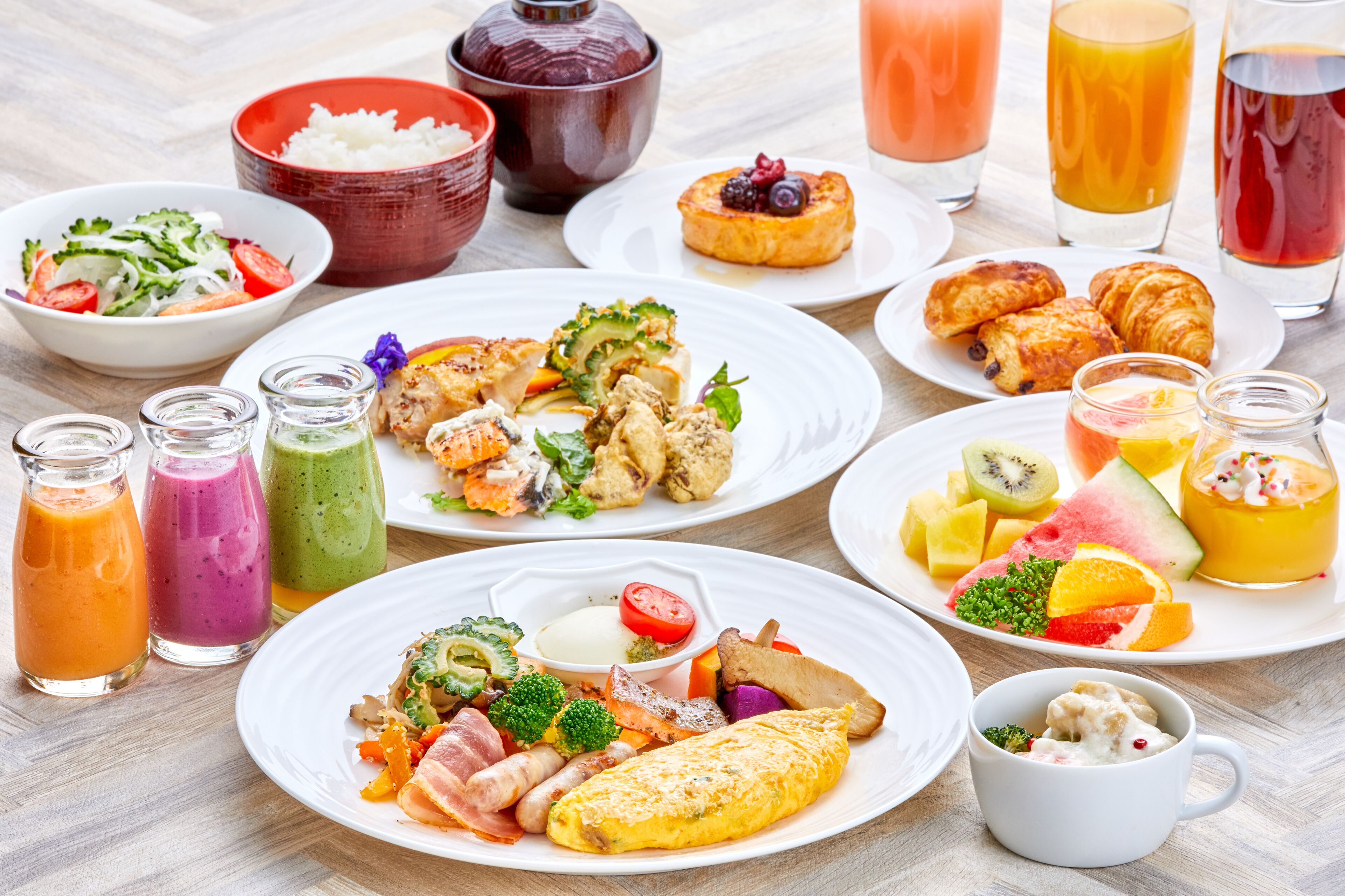 A variety of breakfast dishes including omelets, pastries, and fresh fruits, along with several types of juices and smoothies.