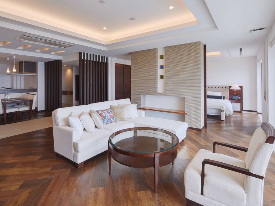 A modern hotel room with a white sofa, a glass coffee table, and a wooden floor.