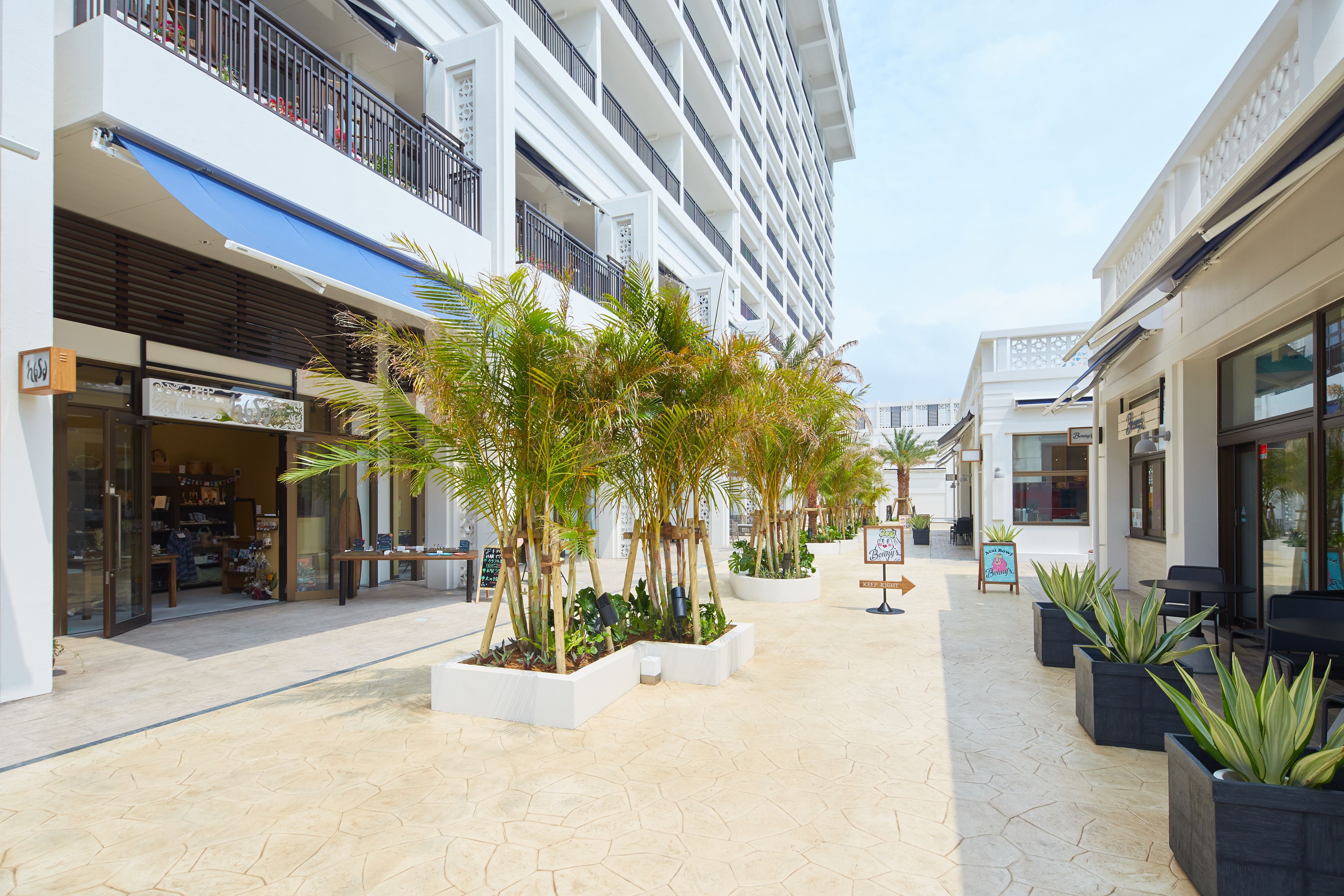 A modern hotel corridor with multiple floors, outdoor seating areas, and potted plants.