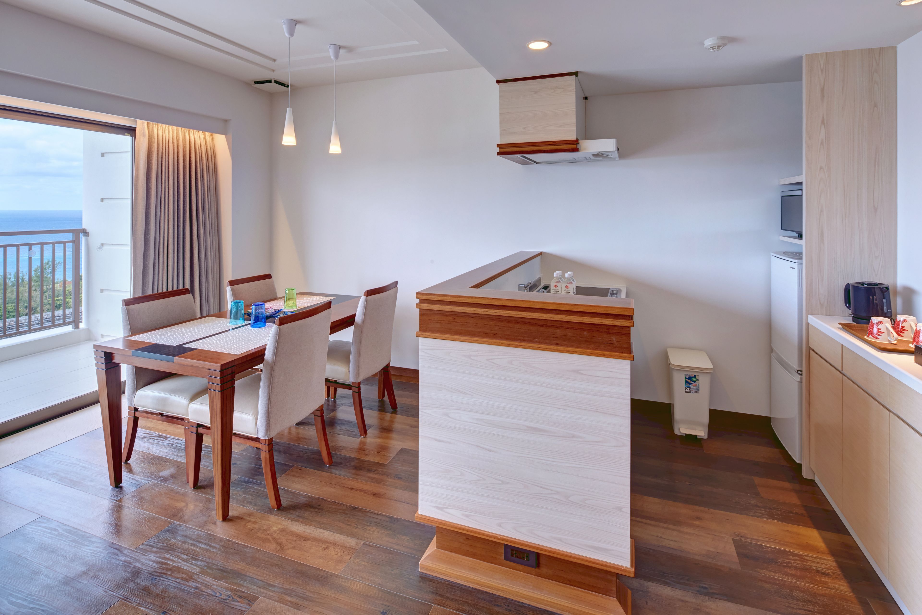 Habitació d'hotel moderna amb zona de menjador, petita cuina i vista al mar.