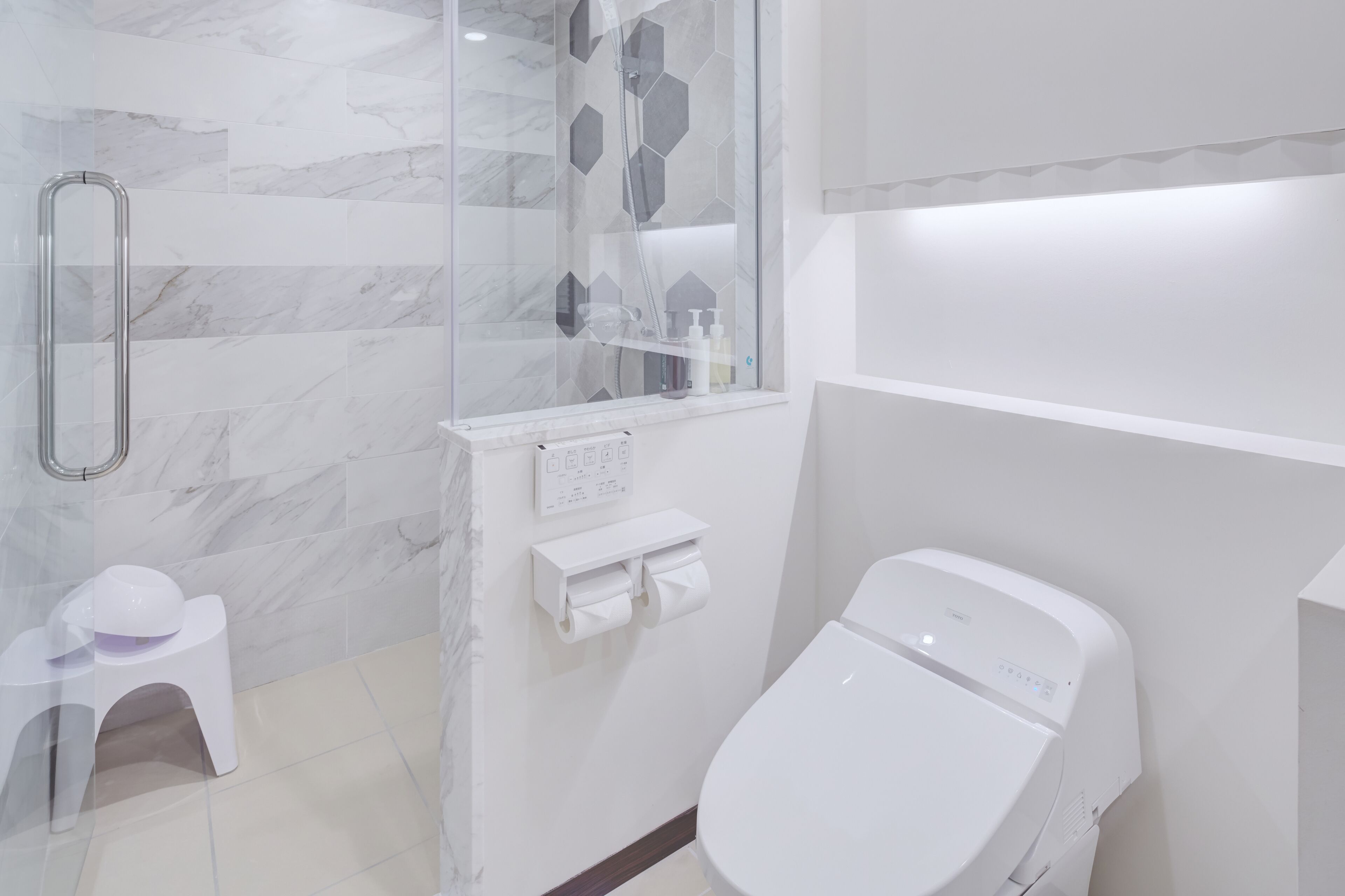 A modern bathroom with a glass shower enclosure, a toilet, and a small white stool.
