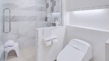 A modern bathroom with a glass shower enclosure, a toilet, and a small white stool.