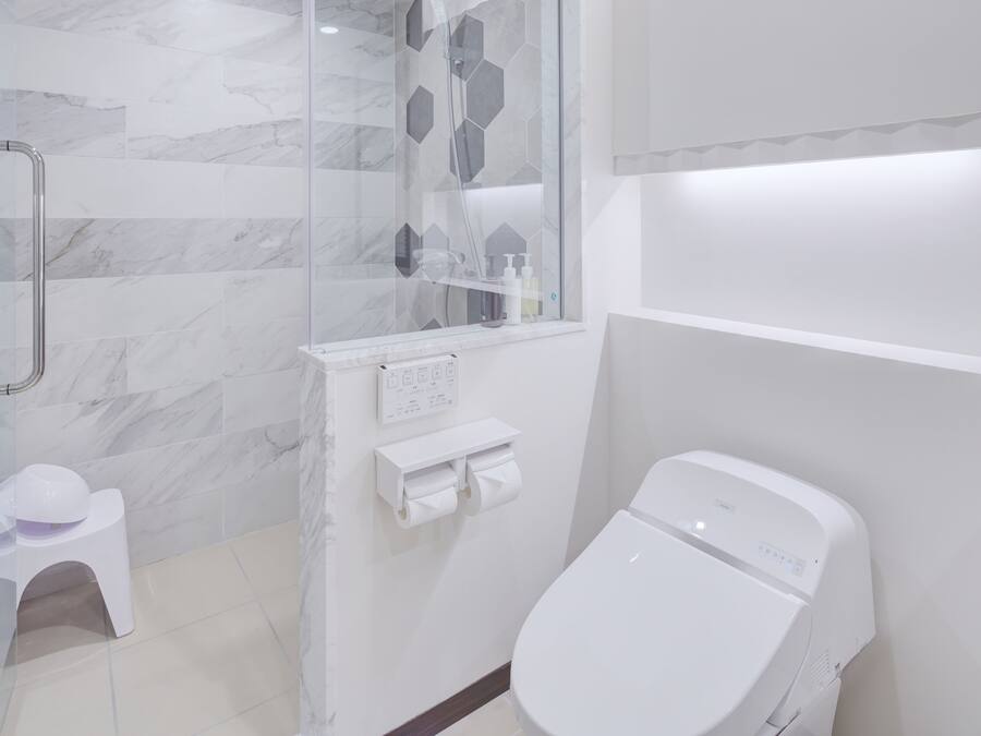 A modern bathroom with a glass shower enclosure, a toilet, and a small white stool.