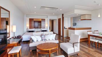 A hotel room with a bed, sofa, dining table, chairs, and a TV.