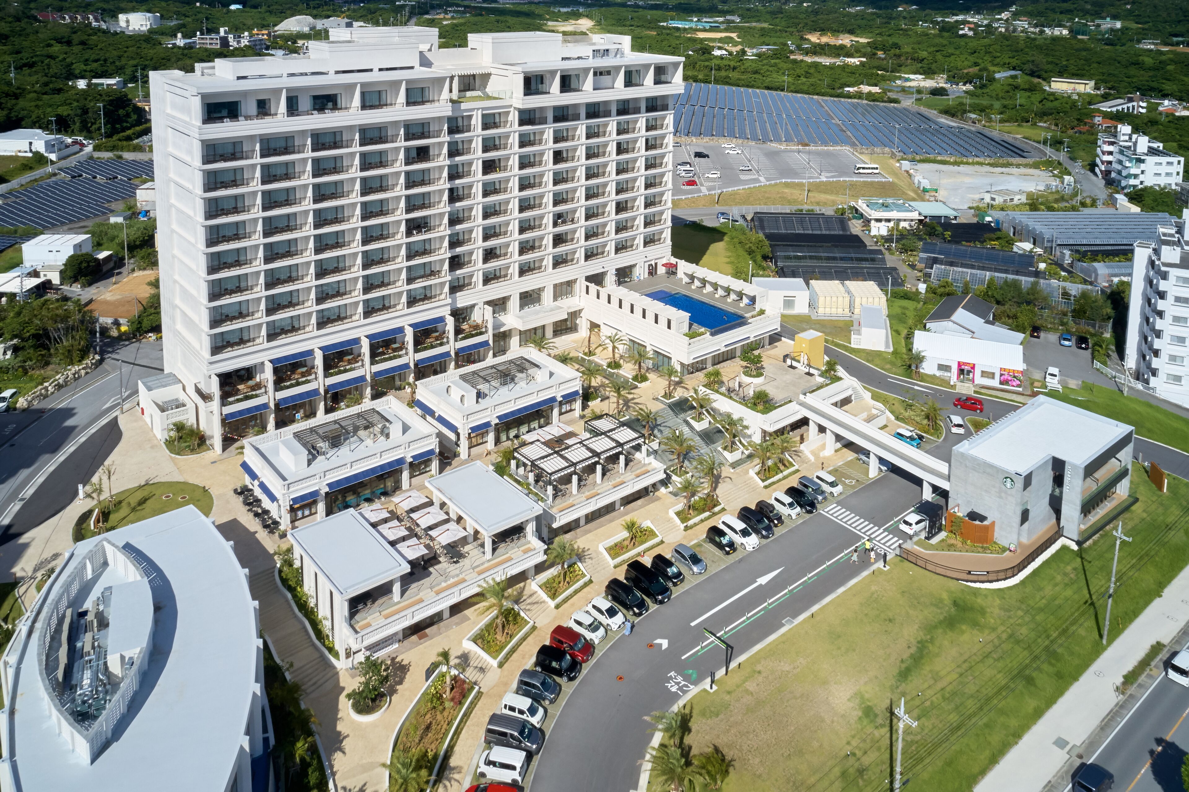 A modern hotel with multiple floors, a parking lot, and solar panels in the background.