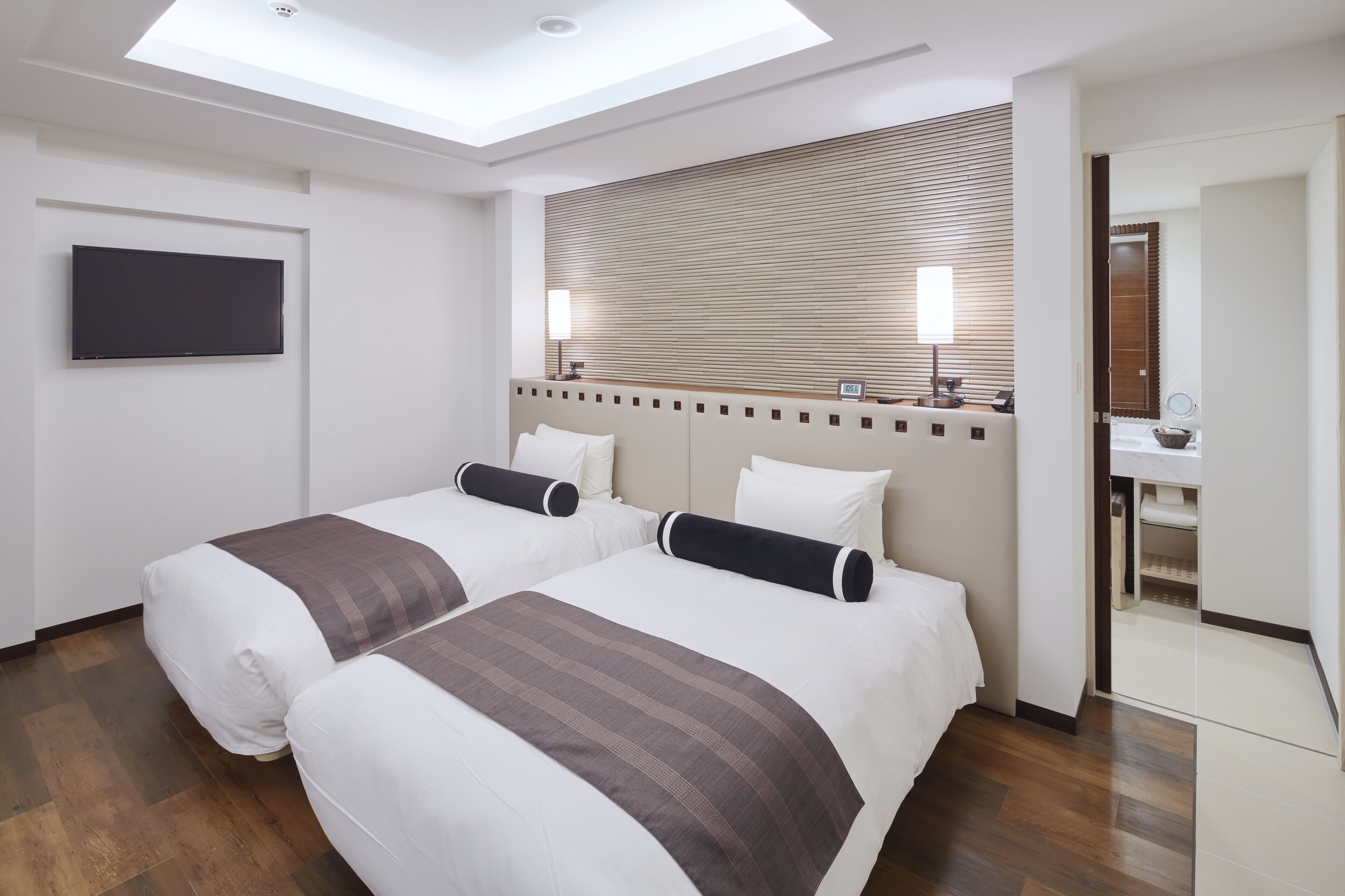A hotel room with two beds, a TV, a wooden headboard, and a bathroom visible through an open door.