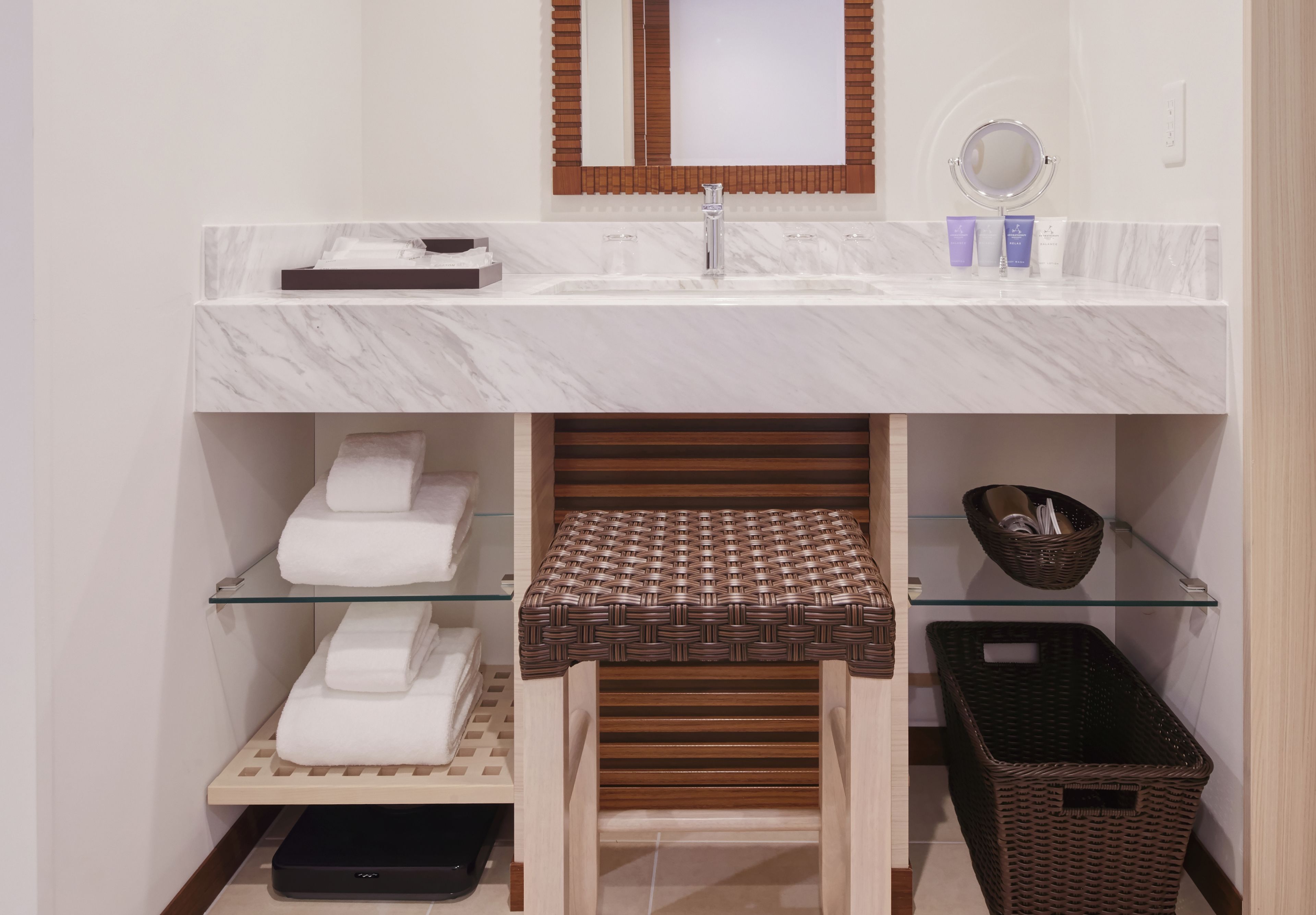 A bathroom with a marble sink, a mirror, a towel rack, and a wicker basket.