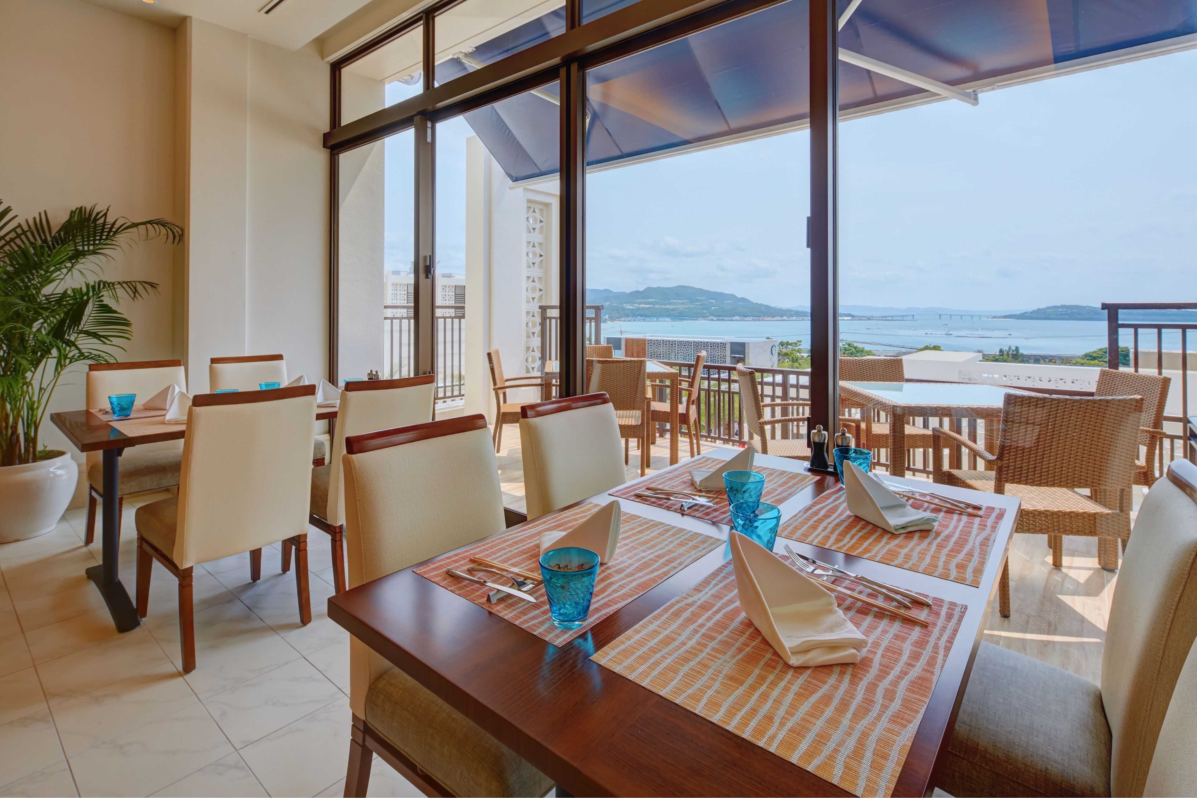 A dining area with tables and chairs, large windows, and a view of the sea.