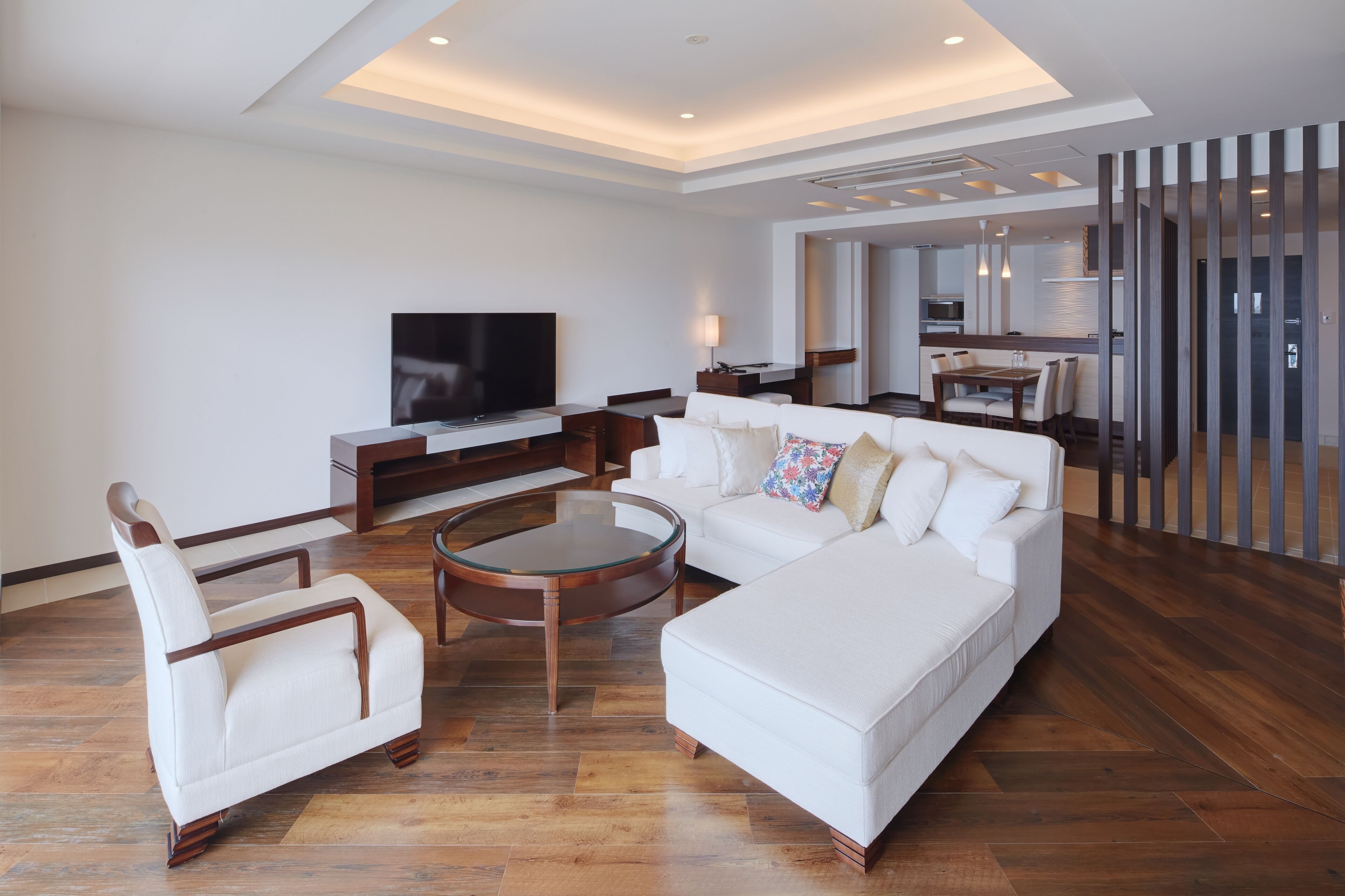 Una sala de estar moderna con un televisor de pantalla plana grande, un sofá blanco, una mesita de centro y una silla de madera.