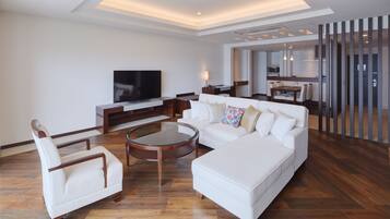 Una sala de estar moderna con un televisor de pantalla plana grande, un sofá blanco, una mesita de centro y una silla de madera.