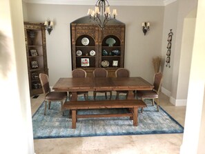 Un comedor con una mesa de madera, seis sillas, un banco, un tapete azul estampado, un aparador decorativo con estantes y apliques de pared.
