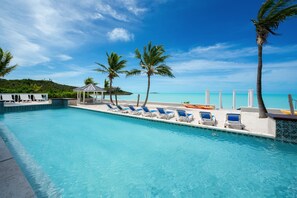 A pool with blue chairs and a gazebo, surrounded by palm trees and a view of the ocean.