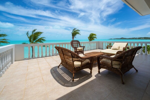 A balcony with wicker furniture, a view of the ocean, and palm trees.
