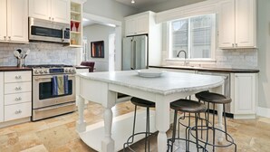 Een moderne keuken met witte kasten, een centraal eiland met krukken, roestvrijstalen apparatuur en een marmeren aanrecht.