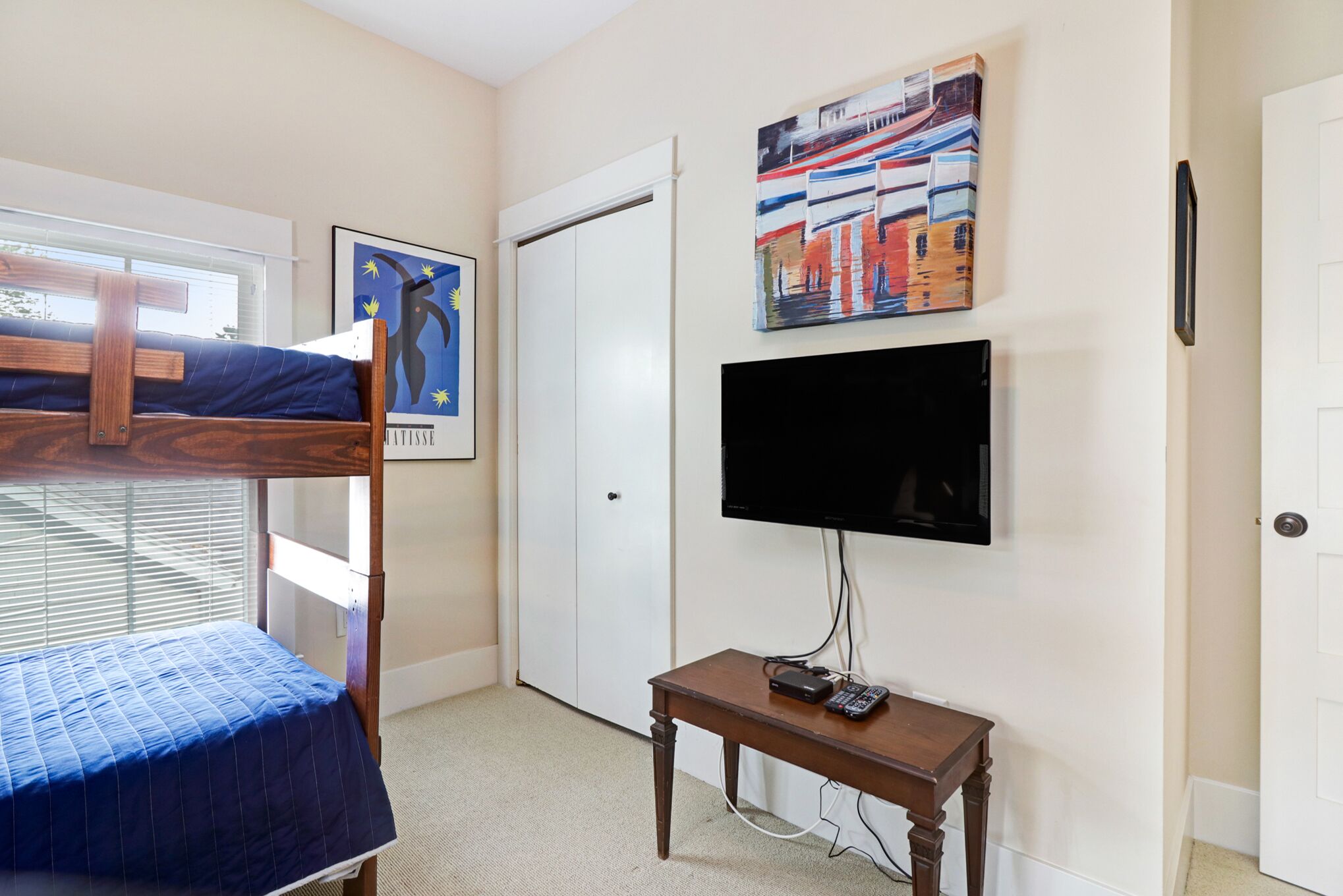 Une chambre avec un lit superposé, un téléviseur fixé au mur et une petite table sur laquelle sont posés des appareils électroniques.