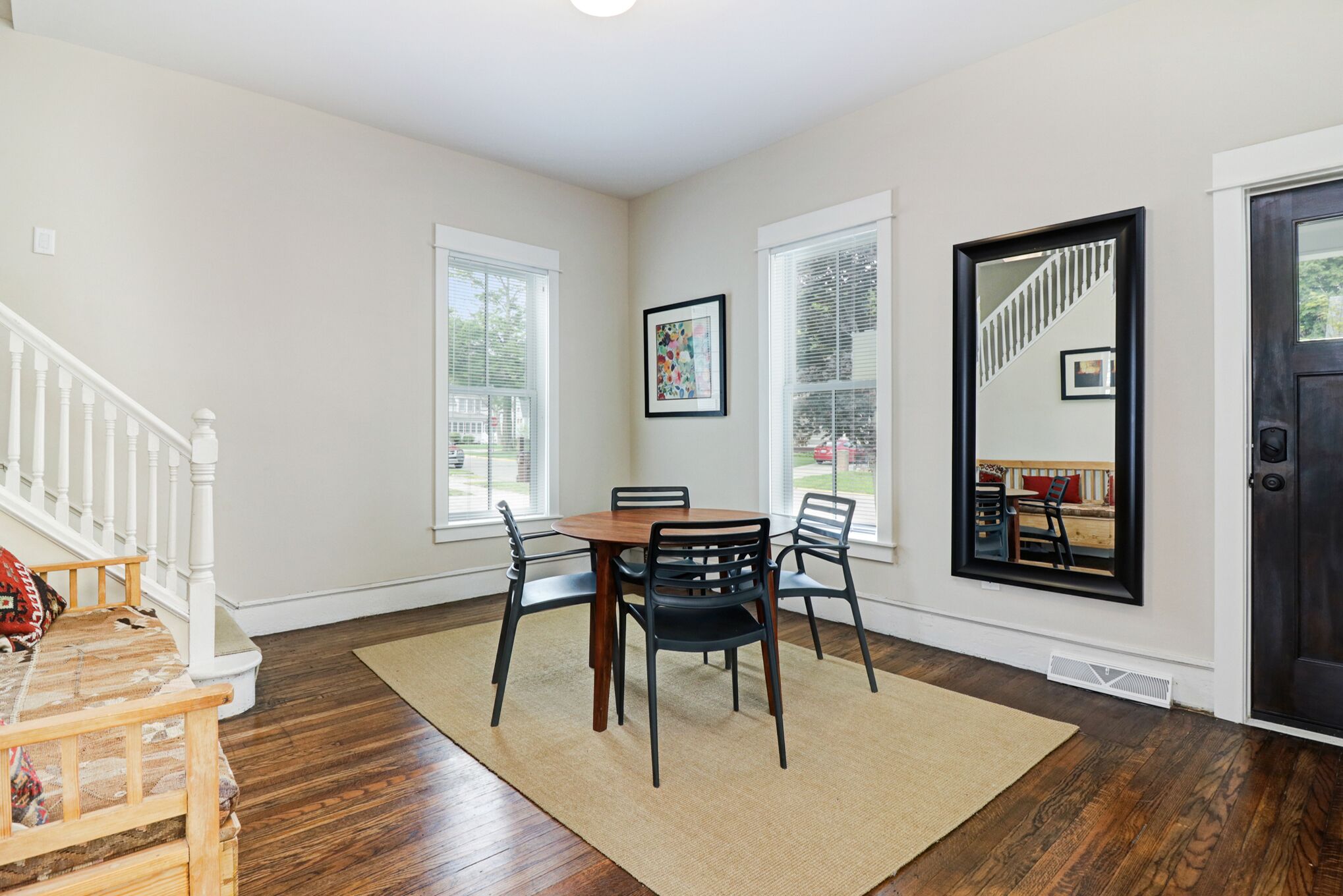 A dining area with a wooden table and chairs, a rug, and a staircase leading to another level.