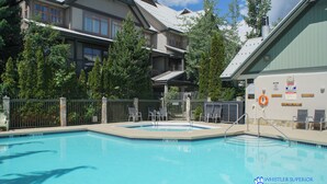 A swimming pool with a fenced deck area, lounge chairs, and a building with multiple balconies in the background. - Central, Whistler Village Family Condo. Pool & Hot Tub, Free Parking & WiFi (Whistler)