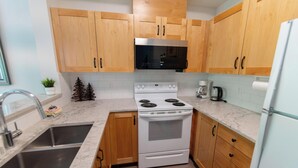 A kitchen with wooden cabinets, a white stove, a microwave, and a stainless steel sink. - Central, Whistler Village Family Condo. Pool & Hot Tub, Free Parking & WiFi (Whistler)