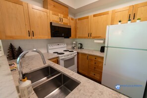 A kitchen with wooden cabinets, a stainless steel sink, a white stove, and a refrigerator. - Stoney Creek Northstar 101 (Whistler)