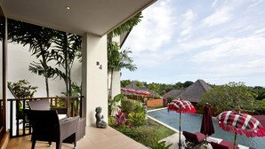 A balcony with wicker furniture, a statue, and a pool area with umbrellas. - 3 Bedroom Sawah Town House B4 Ocean View   (Tabanan)