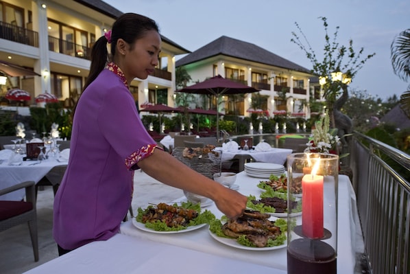 A dining table set outdoors with plates of food, a lit candle, and a person serving.