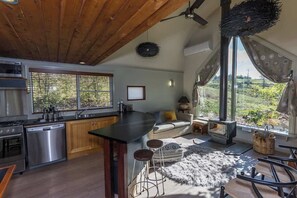 A modern kitchen with a large island, stainless steel appliances, and a view of greenery outside.