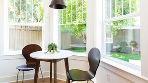 A dining area with a round table and two chairs, a hanging light fixture, and large windows with a view of a backyard. - ~LARGE WESTSIDE HOME~ Walk to everything! Welcome to KINGSTON HOUSE (Bend)