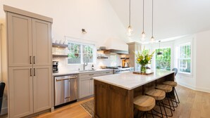 A modern kitchen with a large island, wooden bar stools, and a view of the outdoors. - ~LARGE WESTSIDE HOME~ Walk to everything! Welcome to KINGSTON HOUSE (Bend)
