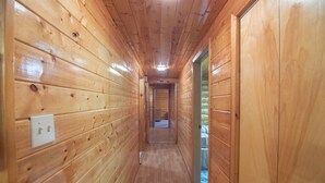 A wooden hallway with a light fixture on the ceiling, a door on the right, and a light switch on the left. - Sashas Place Kenai River Alaskan Log Cabin with HOT TUB - Maintained Daily (Soldotna)