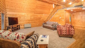 A log cabin interior with a staircase, two sofas, a television, and a table. - Sashas Place Kenai River Alaskan Log Cabin with HOT TUB - Maintained Daily (Soldotna)