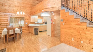 A wooden cabin interior with a dining area, kitchen, and staircase. - Sashas Place Kenai River Alaskan Log Cabin with HOT TUB - Maintained Daily (Soldotna)