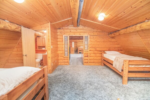 Une chambre située dans une cabane en rondins, avec deux lits en bois, une petite salle de bain et un espace aménagé en mezzanine.