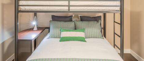 A bunk bed with a desk and lamp, featuring a striped bedspread and pillows.