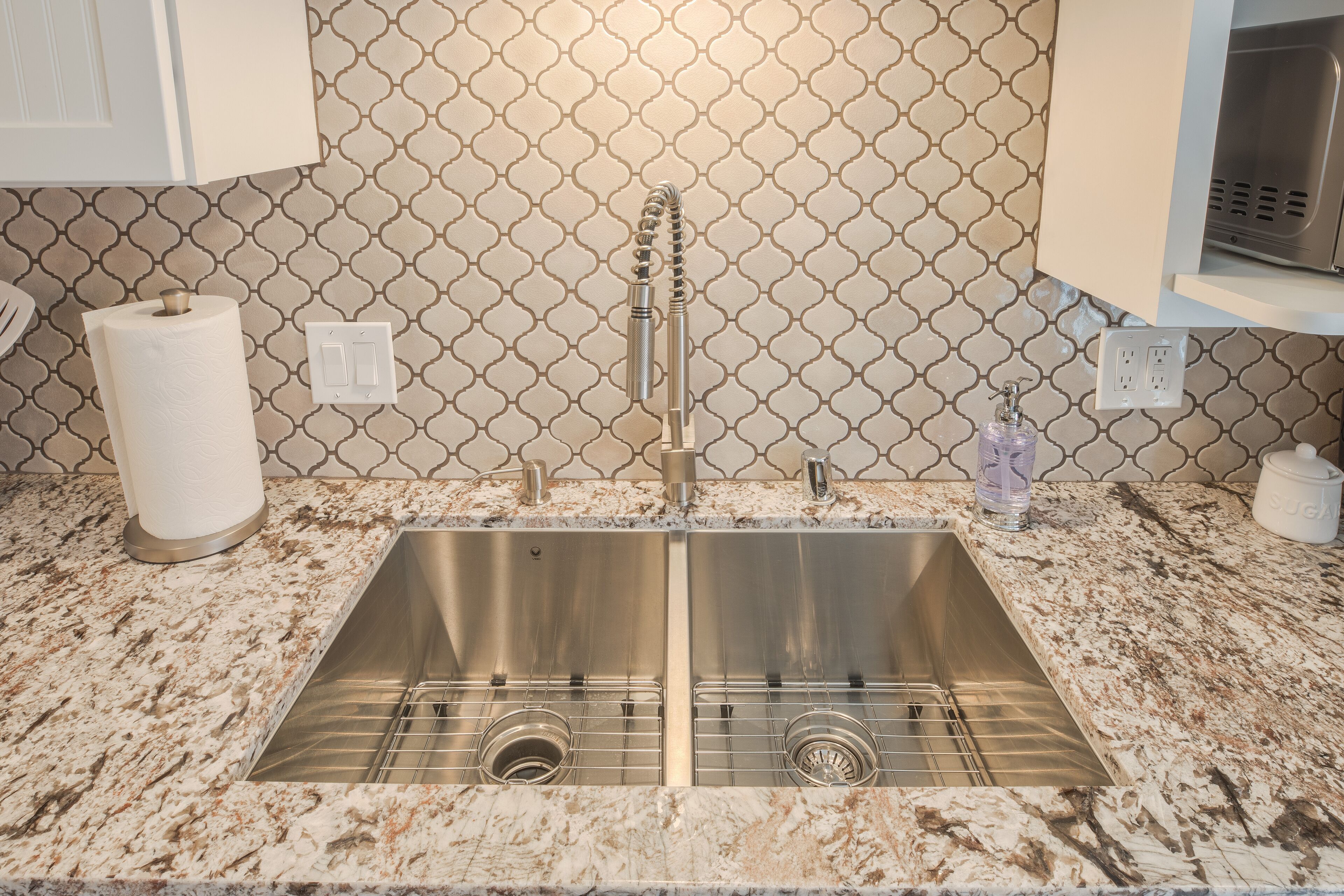 Una cocina con un lavamanos de acero inoxidable, encimera de mármol y salpicadero con diseño.