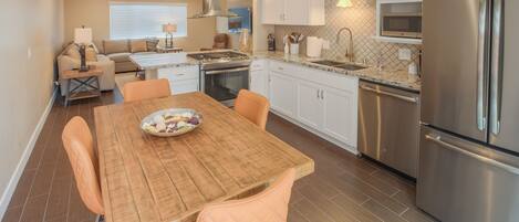 A modern kitchen with white cabinets, stainless steel appliances, and a wooden dining table with orange chairs.